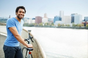 Young man with bike smiling on waterfront pedestrian ramp at dusk.