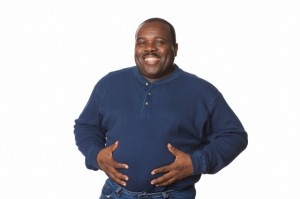 Studio portrait of middle overweight aged African American man on white background looking happy and full with hands on stomach