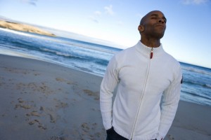 Young man with eyes closed on beach, hands in pockets